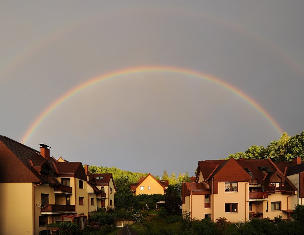 Arco-íris duplo sobre casas, com o céu escuro de chuva