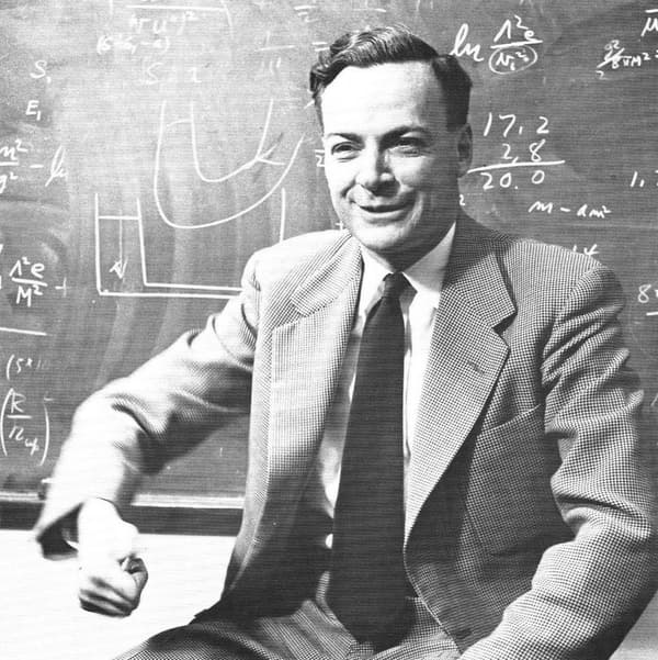 Richard Feynman sorrindo, sentado diante de um quadro cheio de contas