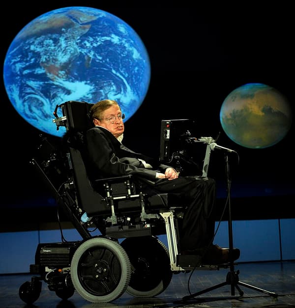 Stephen Hawking em sua cadeira de rodas num palco, com imagens da Terra e de Marte no telão