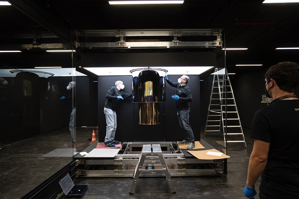 Computador quântico: um cilindro dourado pendurado numa sala escura, com técnicos em volta