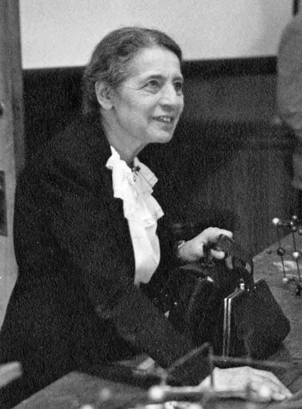 Lise Meitner dando aula, sentada a uma mesa