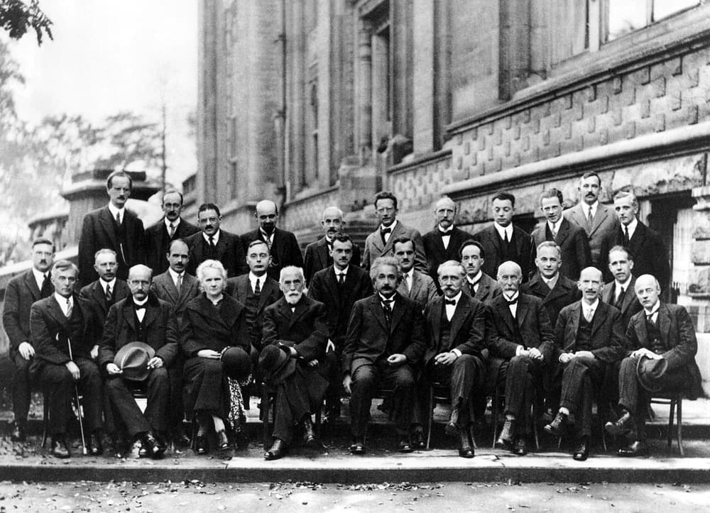 Foto em preto e branco de 29 cientistas de terno em três fileiras, diante de um prédio