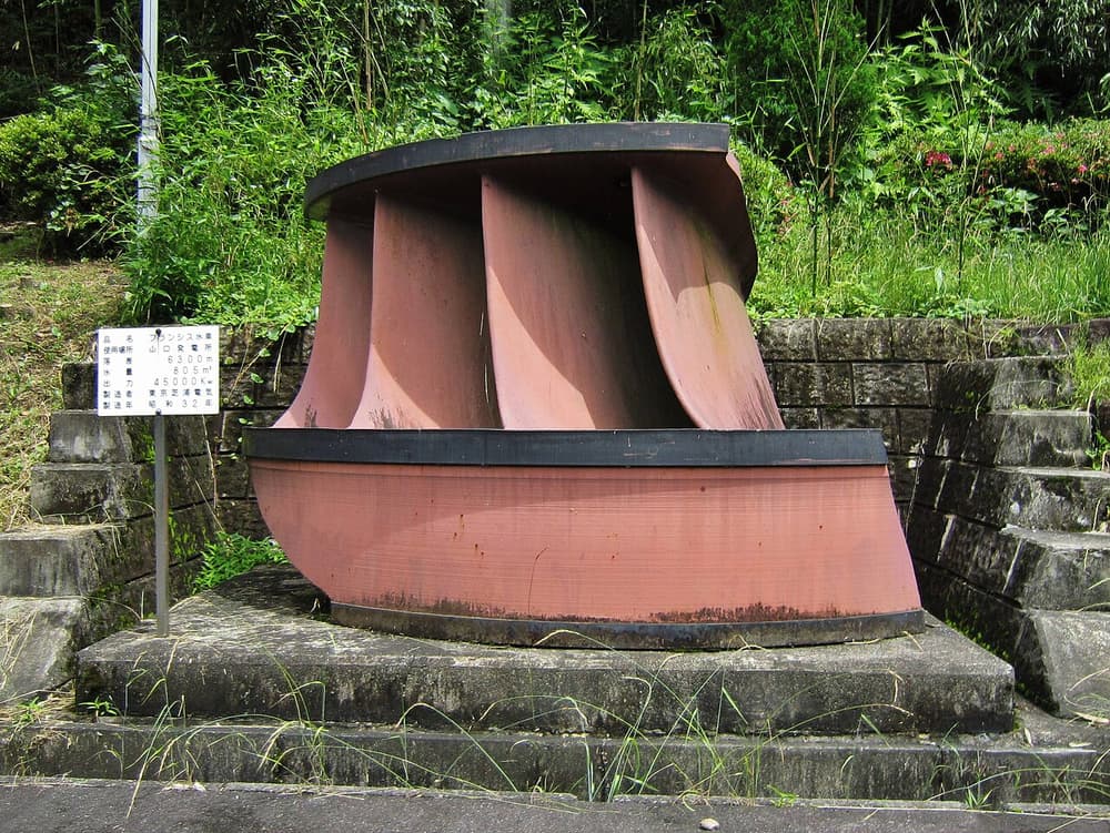 Rotor de turbina Francis antiga, com pás curvas de metal, exposto num jardim