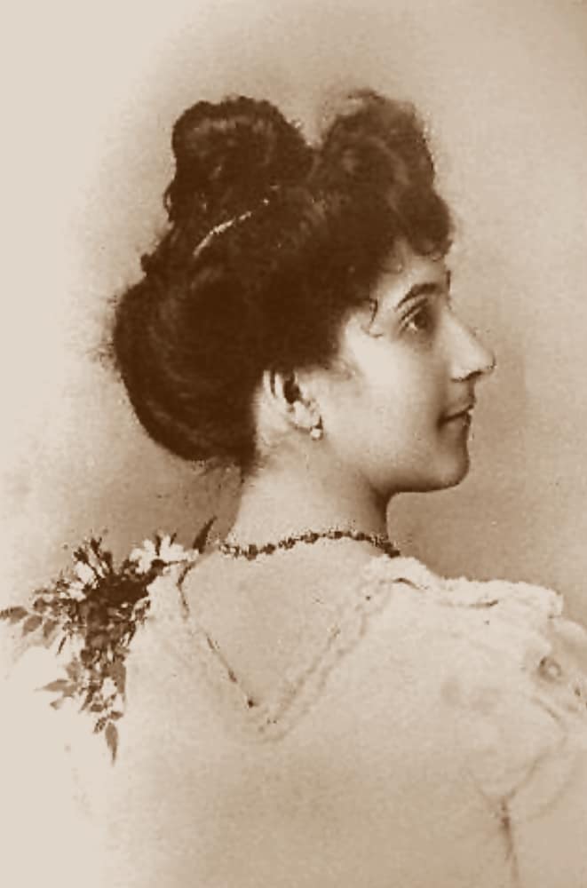 Foto antiga, em tons de sépia, de uma jovem de perfil com o cabelo preso no alto da cabeça
