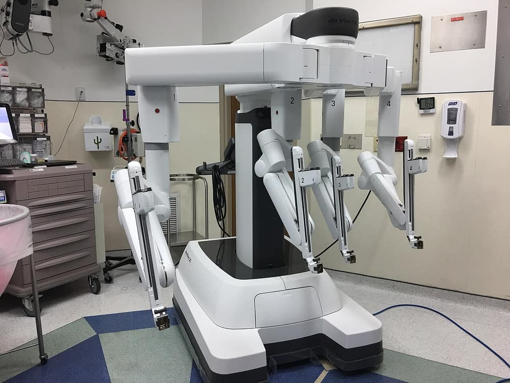Robô cirúrgico branco com quatro braços articulados numa sala de cirurgia