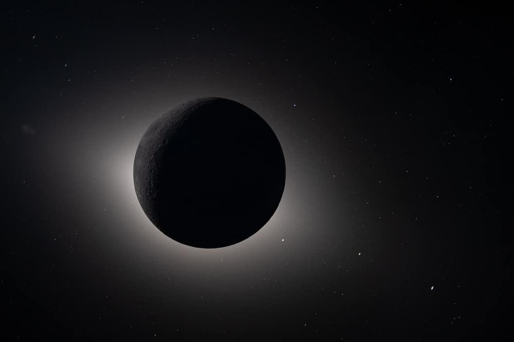 A Lua escura cobrindo o Sol, com um brilho branco em volta, no céu negro