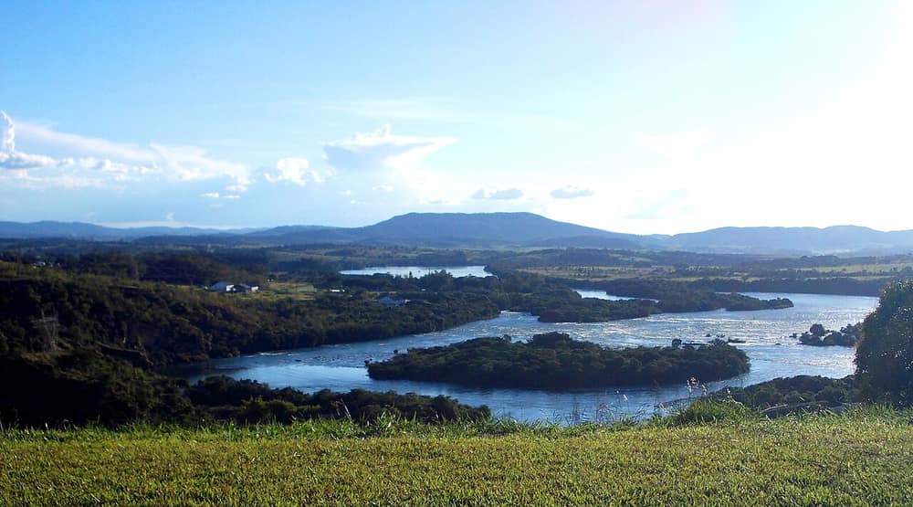 Lago grande com ilhas cobertas de mata, entre morros, num dia de céu azul