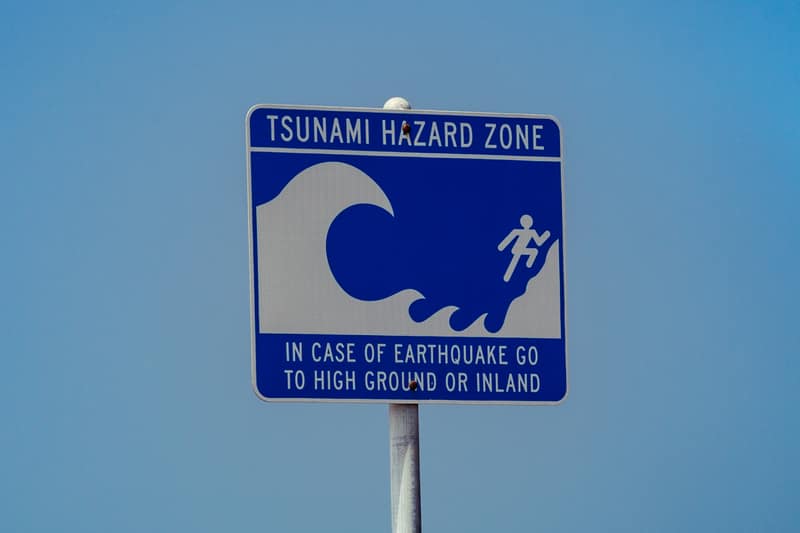 Placa azul e branca de zona de risco de tsunami, com o desenho de uma onda e de uma pessoa correndo