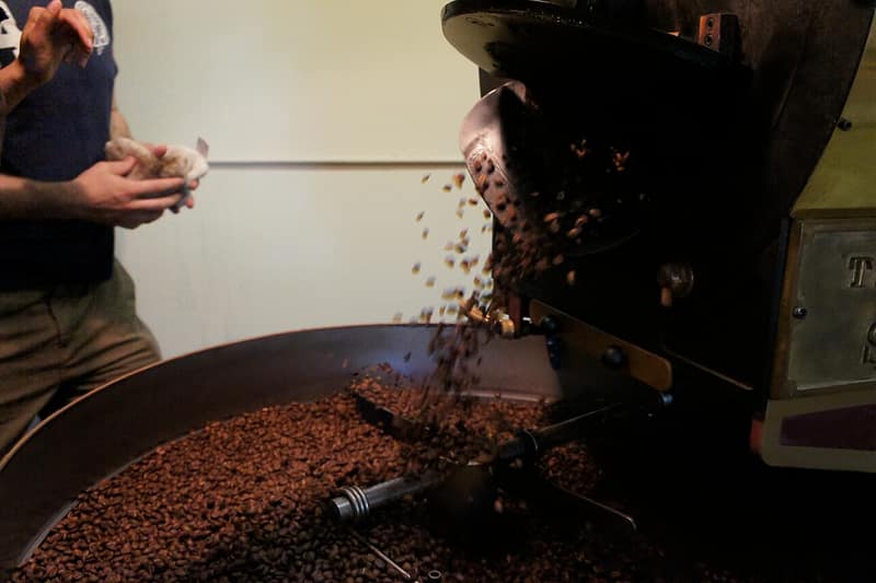 Grãos de café recém-torrados caindo do torrador numa bandeja