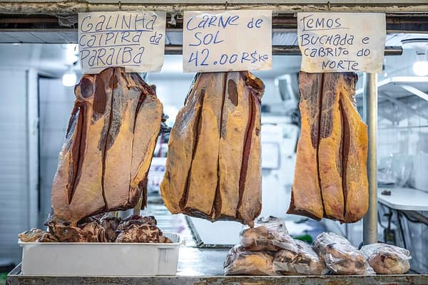 Mantas de carne de sol penduradas num açougue de mercado, com plaquinhas de preço