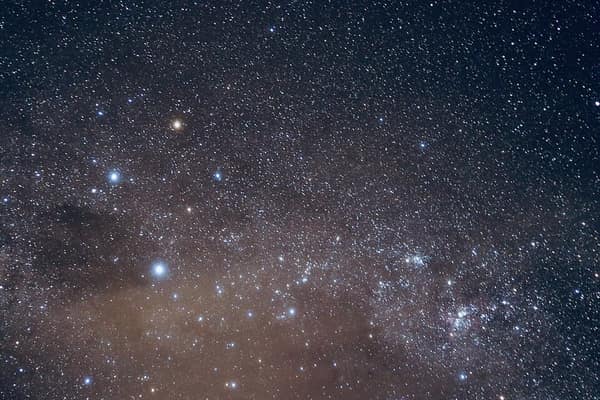 Foto do céu noturno com o Cruzeiro do Sul: uma estrela alaranjada no topo, a estrela mais brilhante embaixo e duas nos braços, sobre a Via Láctea
